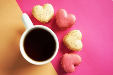 Kalp şeklinde badem kurabiyeleri pembe ve sarı arka planda bir fincan çayın yanında.