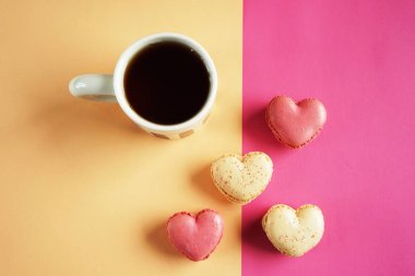 Kalp şeklinde badem kurabiyeleri pembe ve sarı arka planda bir fincan çayın yanında.