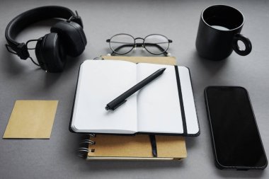 Not defterleri kalem, yapışkan notlar, bir fincan kahve, bardak, akıllı telefon ve gri arka plandaki kulaklıklar.