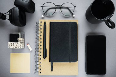 Not defterleri kalem, yapışkan notlar, bir fincan kahve, bardak, akıllı telefon ve gri arka plandaki kulaklıklar.