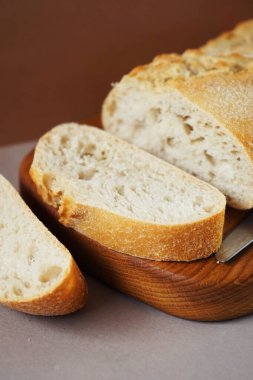 Tahtadaki buğday ciabatta kahverengi-gri arka planda bir bıçağın yanında.