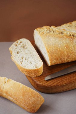 Tahtadaki buğday ciabatta kahverengi-gri arka planda bir bıçağın yanında.