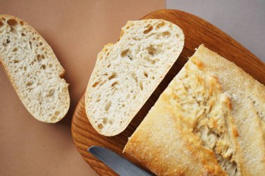 Tahtadaki buğday ciabatta kahverengi-gri arka planda bir bıçağın yanında.