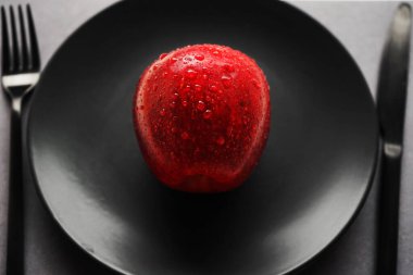 Mutfak eşyalarının yanında siyah bir tabakta kırmızı elma.