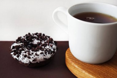 Beyaz jöleli çikolatalı çörek beyaz ve kahverengi arka planda beyaz bir fincan kahvenin yanında çikolata parçacıklı.