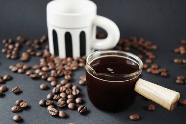 Koyu arkaplanda bir fincan kahvenin yanında bir bardak kepçe.