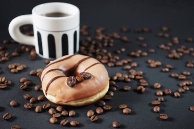 Koyu arkaplanda bir fincan sade kahvenin yanında kahve süslemeli karamel çörek.