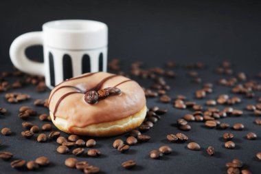 Koyu arkaplanda bir fincan sade kahvenin yanında kahve süslemeli karamel çörek.