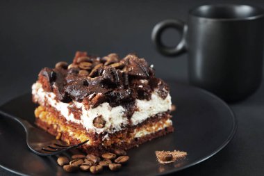 Siyah tabakta kahve aromalı çikolatalı kek, koyu arkaplanda bir fincan kahvenin yanında.