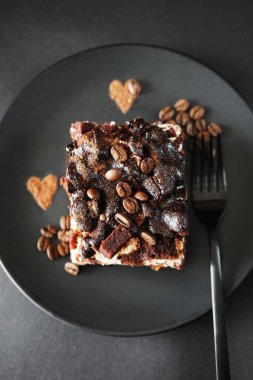 Siyah bir tabakta kahve aromalı çikolatalı kek, arka planda bir çatalın yanında.