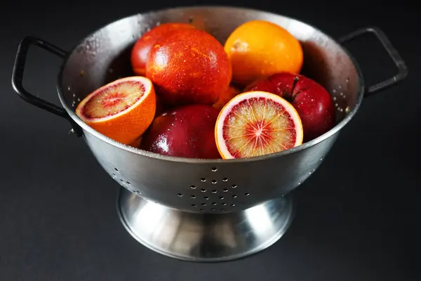 Apples and blood oranges in a metal colander on a dark background