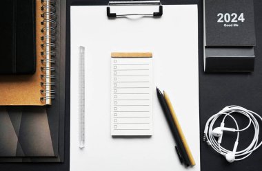 Koyu arkaplanda klasörlerin, not defterlerinin, kalemlerin, takvimin ve kablo kulaklıkların yanında kağıt tutucu