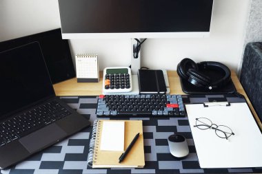 Not defterleri, dizüstü bilgisayarı, monitörü, klavyesi, faresi, kulaklığı olan bir masaüstü