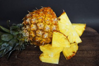 Koyu arkaplanda tahta bir tahtada parçaları kesmek için yanında olgun sulu bir ananas.