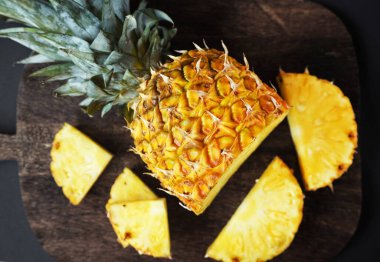 Koyu arkaplanda tahta bir tahtada parçaları kesmek için yanında olgun sulu bir ananas.
