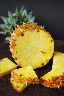 Koyu arkaplanda tahta bir tahtada parçaları kesmek için yanında olgun sulu bir ananas.