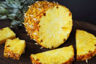 Koyu arkaplanda tahta bir tahtada parçaları kesmek için yanında olgun sulu bir ananas.