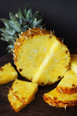 Koyu arkaplanda tahta bir tahtada parçaları kesmek için yanında olgun sulu bir ananas.