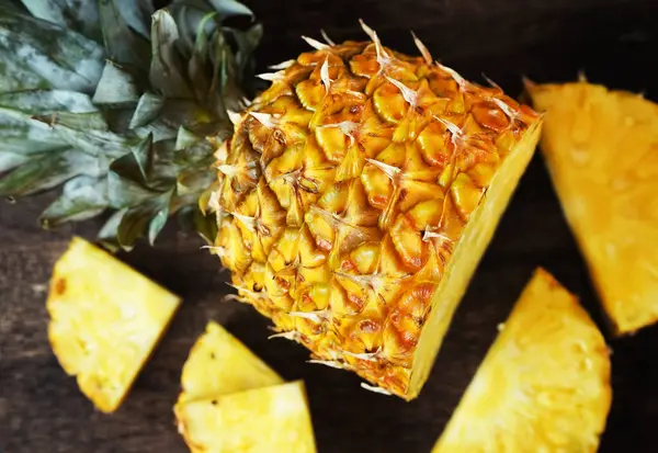 Koyu arkaplanda tahta bir tahtada parçaları kesmek için yanında olgun sulu bir ananas.