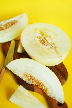 Sarı bir zemin üzerinde tahta bir tahtada dilimlenmiş olgun sarı kavun.