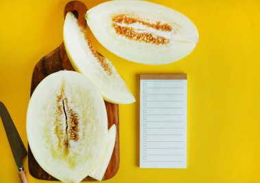 Tahtada dilimlenmiş sarı kavun, sarı arka planda boş bir listenin yanında.