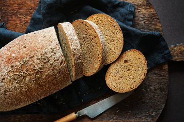 Taze dilimlenmiş siyah tahıl ekmeği. Koyu arkaplanda tahta üzerinde bir bıçağın yanında.