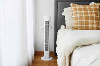 Beyaz kule pervanesi modern, parlak yatak odasında yatağın yanında.