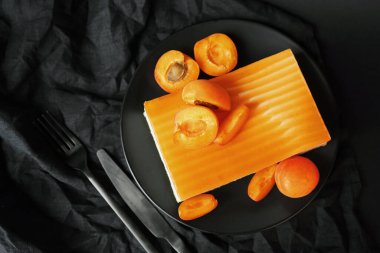 Krema ve kayısı reçelinden yapılmış kek siyah bir tabakta kayısı reçelinin yanında.