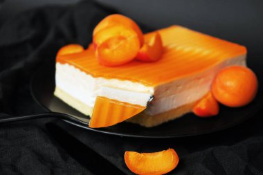 Krema ve kayısı reçelinden yapılmış kek siyah bir tabakta kayısı reçelinin yanında.