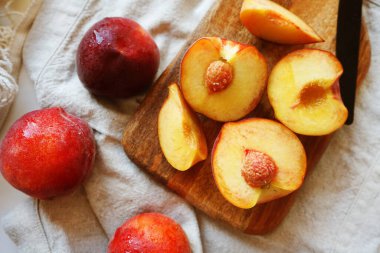 Tahtada olgun şeftaliler ve arka planda bir bıçak ve ip torbasının yanında keten bir peçete.