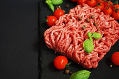 Koyu arkaplanda kiraz domatesleri, fesleğen ve baharatların yanında siyah bir tepside taze kıyma.