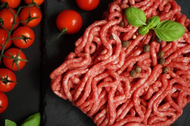 Koyu arkaplanda kiraz domatesleri, fesleğen ve baharatların yanında siyah bir tepside taze kıyma.