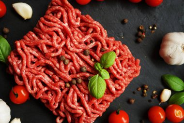 Sarımsak, kiraz domatesleri, fesleğen ve baharatların yanında siyah bir tepside taze kıyma.