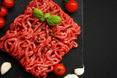 Sarımsak, kiraz domatesleri, fesleğen ve baharatların yanında siyah bir tepside taze kıyma.