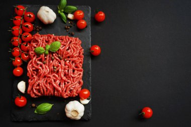 Sarımsak, kiraz domatesleri, fesleğen ve baharatların yanında siyah bir tepside taze kıyma.