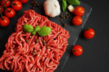 Sarımsak, kiraz domatesleri, fesleğen ve baharatların yanında siyah bir tepside taze kıyma.