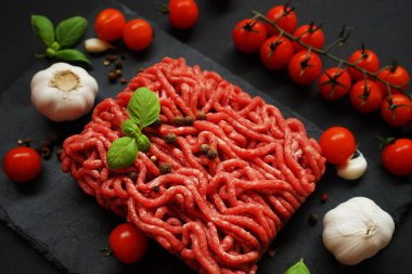 Sarımsak, kiraz domatesleri, fesleğen ve baharatların yanında siyah bir tepside taze kıyma.