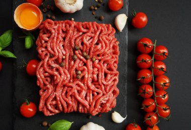 Sarımsak, kiraz domatesleri, fesleğen ve baharatların yanında siyah bir tepside taze kıyma.