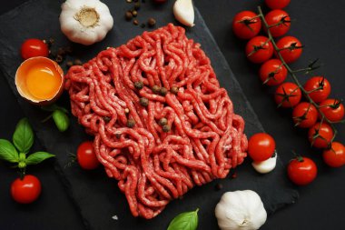 Sarımsak, kiraz domatesleri, fesleğen ve baharatların yanında siyah bir tepside taze kıyma.