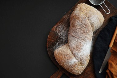 Tahtadaki taze ekmek, arka planda keten peçeteli bıçağın yanında.