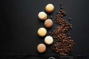 Siyah fincanın yanında kahve çekirdekleri ve siyah arka planda makaronlar.