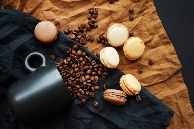 Siyah fincanın yanında kahve çekirdekleri ve koyu arkaplanda siyah ve kahverengi havlular.