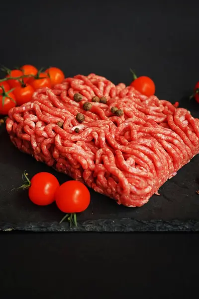 stock image Fresh minced meat on a black slate tray next to cherry tomatoes and spices on a dark background