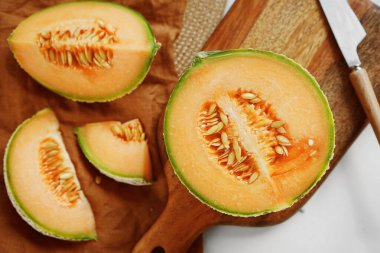 Olgun sarı kavun, tahta bir tahtada bir bıçak ve keten peçetenin yanında dilimlenmiş.