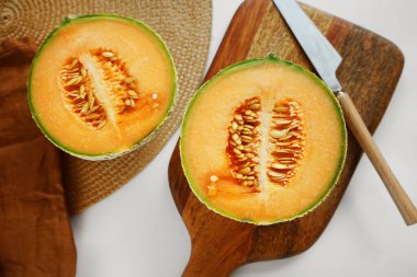 Olgun sarı kavun, tahta bir tahtada bir bıçak ve keten peçetenin yanında dilimlenmiş.