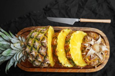 Olgun ananas, tahta tepside dilimlenmiş, koyu arkaplanda bir bıçağın yanında.