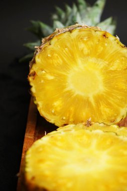 Olgun ananas, koyu bir arka planda tahta bir tepside dilimlenmiş.