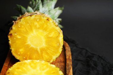 Olgun ananas, koyu bir arka planda tahta bir tepside dilimlenmiş.