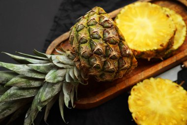 Olgun ananas, koyu bir arka planda tahta bir tepside dilimlenmiş.