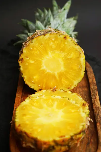 Olgun ananas, koyu bir arka planda tahta bir tepside dilimlenmiş.